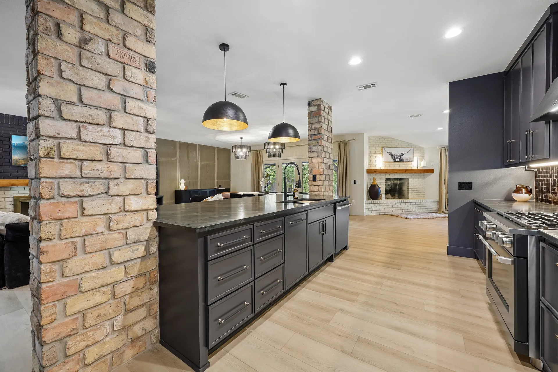 Wild Oak kitchen with charcoal cabinetry, warm brick columns, and brass pendant lights